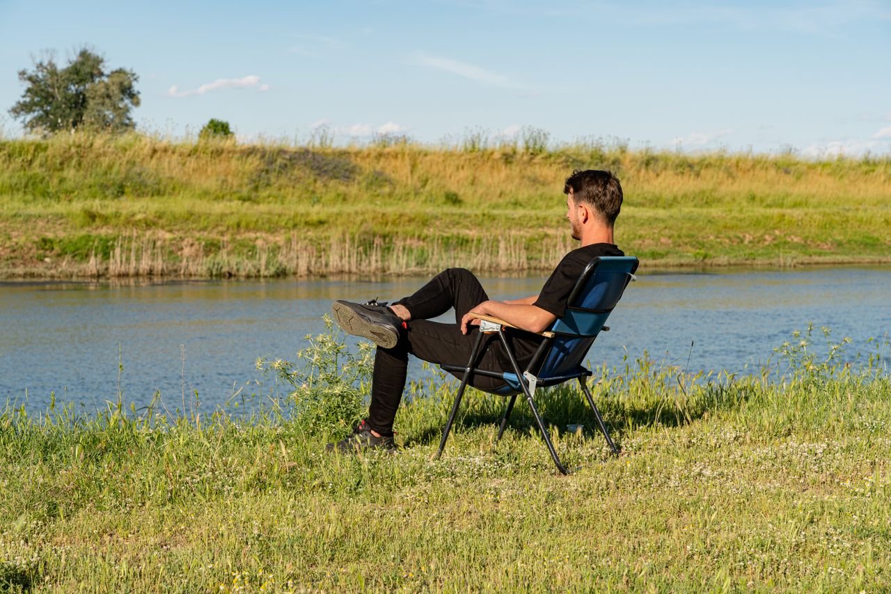 A man in casual attire enjoys a peaceful moment sitting by a tranquil river.